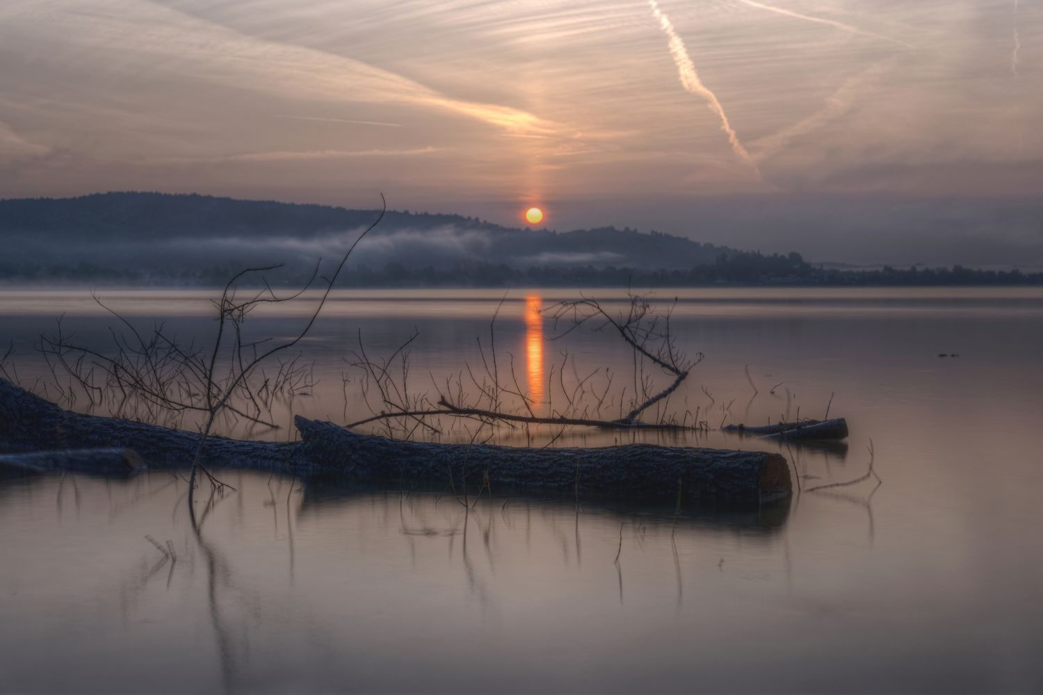 Quiet morning light over calm water with distant hills on the horizon
