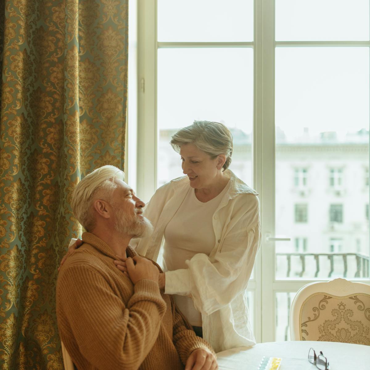 A mature couple smiling together by a warm sunlit window at Ascend Mind and Body — senior-focused primary care in Tampa and Wesley Chapel