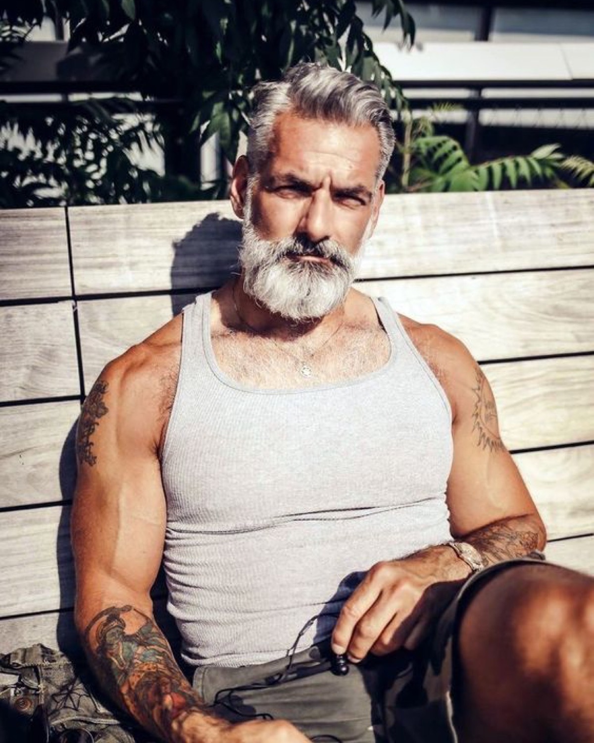 A fit silver-haired bearded man in his fifties seated outdoors in a tank top with sunlight on his shoulders, representing men&rsquo;s health, testosterone, and preventive care at Ascend Mind and Body.