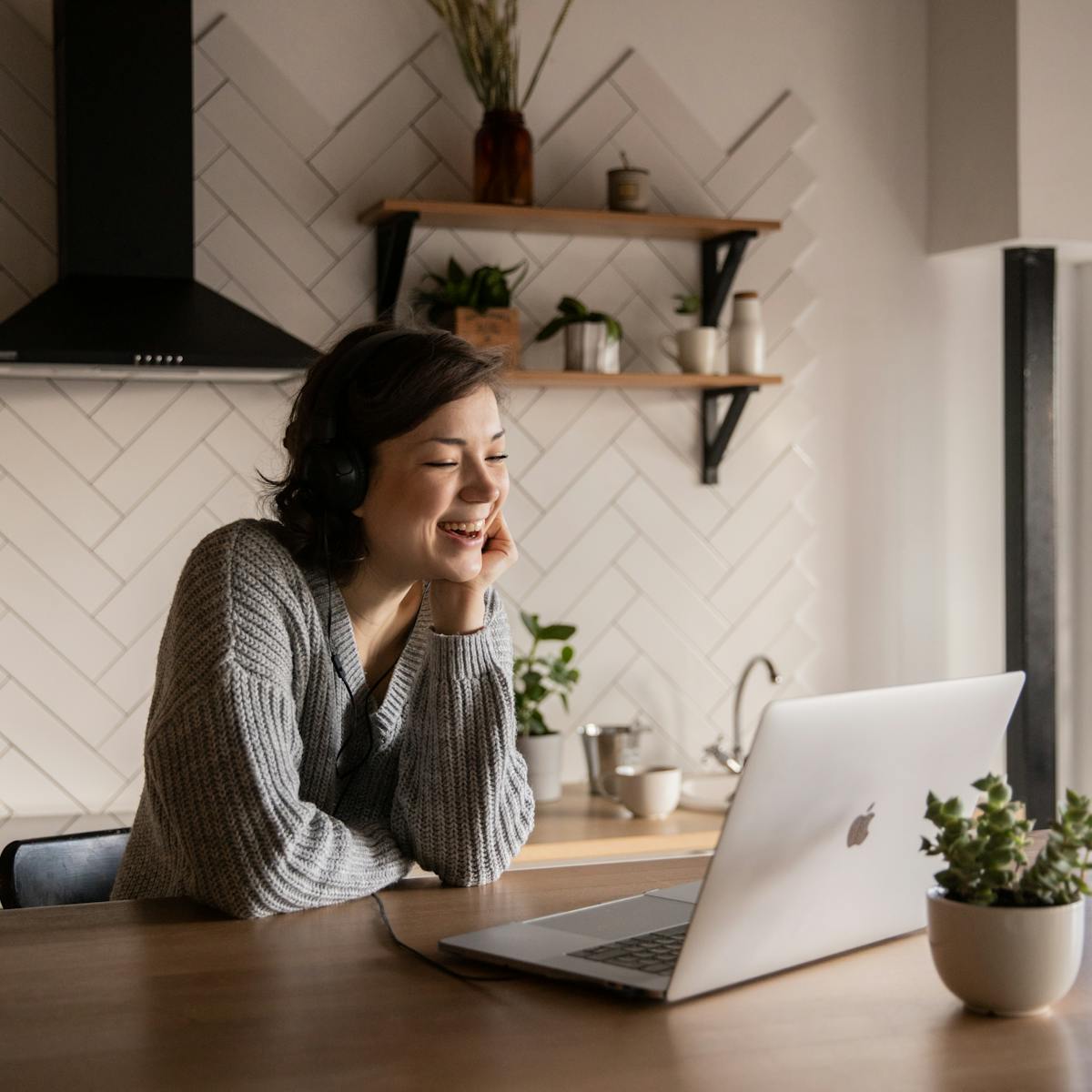 A smiling woman on a laptop video-therapy call in a bright, plant-filled room - representing accessible talk therapy at Ascend Mind and Body